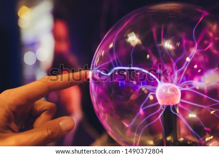 Hand touching a plasma ball with smooth magenta-blue flames. Royalty-Free Stock Photo #1490372804