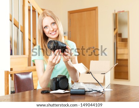 Cute young  girl unpacking new digital camera  in home interior at the table 
