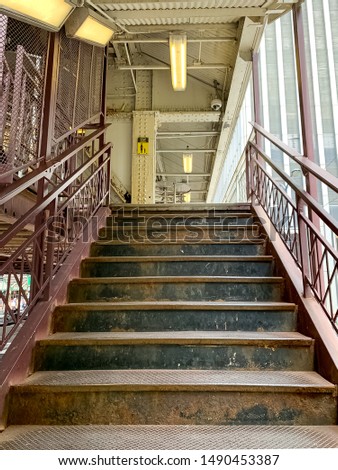 Empty and rusty stairway leading up to an elevated "el" train station platform, with view of sign saying "Hold Onto Your Children".