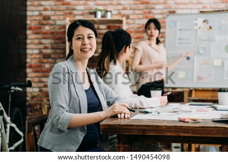 three business people sitting and discussing at meeting in modern office. group of young female coworkers talking about new project in board room. smiling pregnant lady face camera looking confident.
