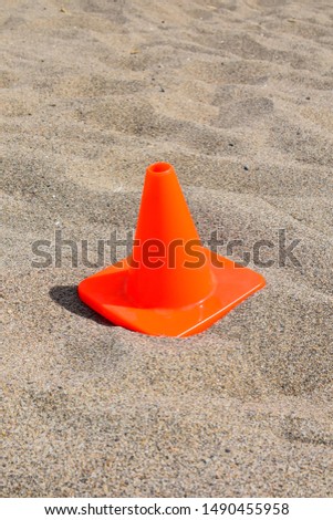 one orange vibrant miniature caution cone isolated in the sand