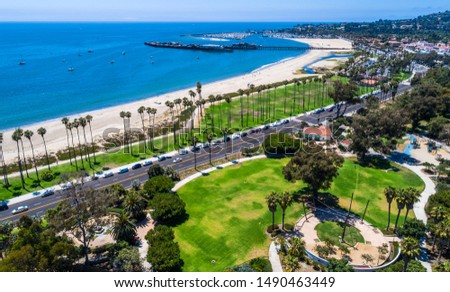 aerial drone view above Santa Barbara , California green central California Beach Town with rows of Tall Palm trees and a sandy beach cove with pier and entire city in the background with mountains
