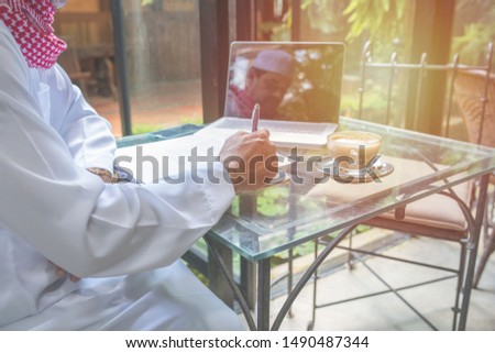 Arab muslim businessman working and writing with notebook on table in coffee shop,freelance business concept.