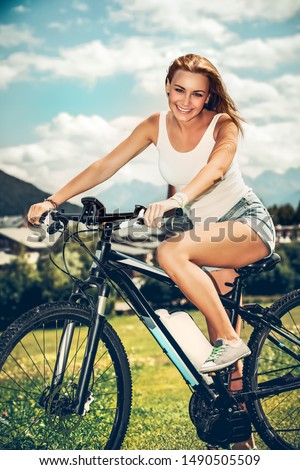 Enjoying bicycle travel in the valley in Alpine mountains, happy woman riding on bike in mountainous countryside, sportive active lifestyle