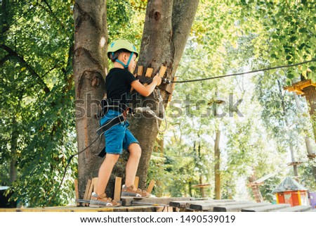 young boy passing the cable route high among trees, extreme sport in adventure park