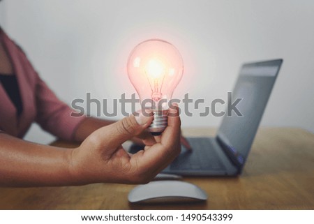 business woman hand holding light bulb with using laptop in office. concept saving energy power