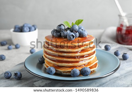 Plate of delicious pancakes with fresh blueberries and syrup on grey table against light background Royalty-Free Stock Photo #1490589836