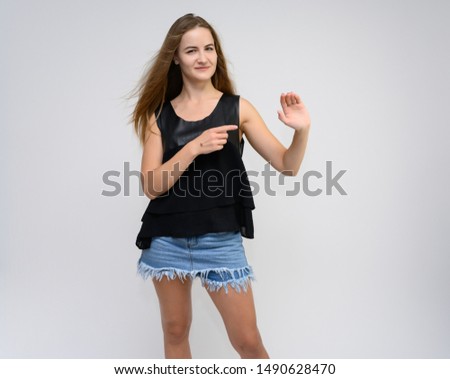 Studio photo portrait of a pretty student girl, young brunette woman with long beautiful hair in denim shorts and a black T-shirt on a white background. Smiling, talking, showing emotions