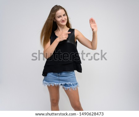 Studio photo portrait of a pretty student girl, young brunette woman with long beautiful hair in denim shorts and a black T-shirt on a white background. Smiling, talking, showing emotions