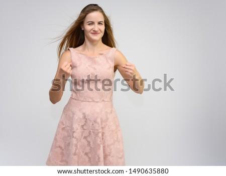 Studio portrait of a knee-length of a pretty girl student, brunette young woman with long beautiful hair in a pink dress on a white background. Smiling, talking, showing emotions
