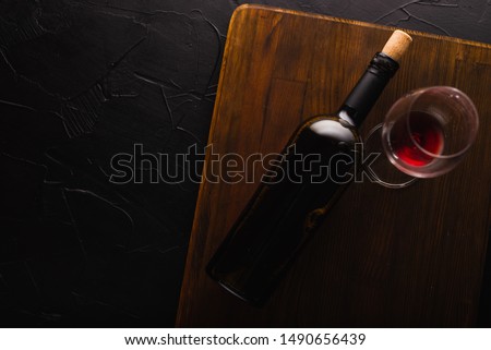 Bottle of red wine with label on old board. Glass of wine and cork