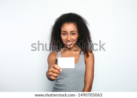 Portrait of beautiful African-American woman with blank business card on light background