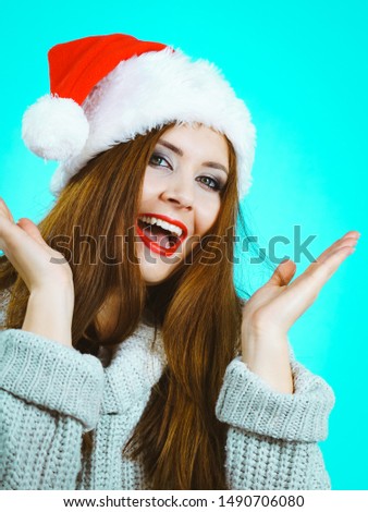 Funny happy surprised, young woman wearing Santa Claus red hat having fun. Pretty lady is ready for Christmas Holiday season. Blue background.