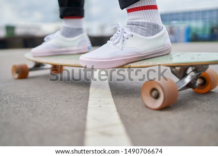 Photo of woman's legs in white sneakers riding skateboard on street in city