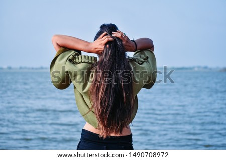 Beautiful Indian model standing in front of lake and tying hair with hands at Nyari dam, Rajkot, India. Royalty-Free Stock Photo #1490708972