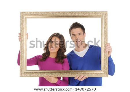 Happy couple in frame. Beautiful young couple looking through a picture frame and smiling while isolated on white