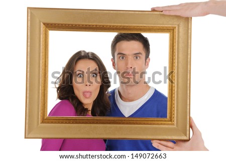 Funny people in frame. Beautiful young couple looking through a picture frame and grimacing while isolated on white