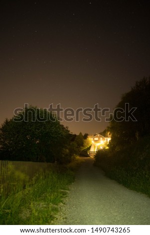 wooden and concrete house at the end of a little road under a night starry sky