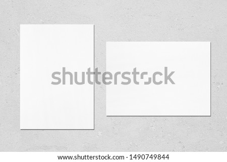 Two empty white vertical and horizontal rectangle poster mockups with soft shadows on neutral light grey concrete background. Flat lay, top view
