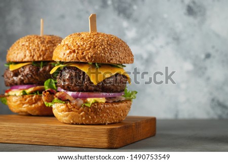 A set of homemade delicious burgers of beef, bacon, cheese, lettuce and tomatoes on a light concrete background. Fat unhealthy food close-up. With copy space.