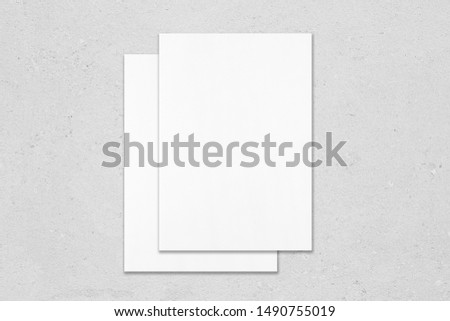 Two empty white rectangle poster mockups lying on top of each other with soft shadows on neutral light grey concrete background. Flat lay, top view