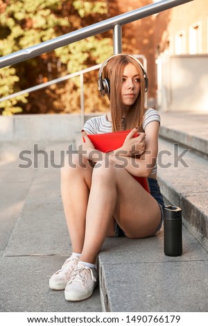 Back to school concept. Beautiful Student blonde girl studying at the stairs with headphones .