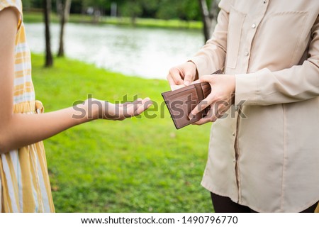 Closeup hands of asian woman hands open wallet,mother or guardian giving pocket money to daughter in green nature,child girl demanding money,allowance,parent pulls out money from wallet to give her Royalty-Free Stock Photo #1490796770