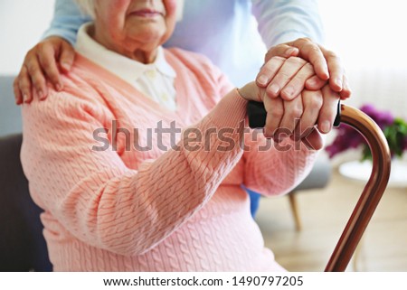 Mature female in elderly care facility gets help from hospital personnel nurse. Senior woman w/ aged wrinkled skin & care giver, hands close up. Grand mother everyday life. Background, copy space.
