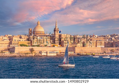 White yacht and Old town of Valletta with churches of Our Lady of Mount Carmel and St. Paul's Anglican Pro-Cathedral at sunset, Valletta, Capital city of Malta