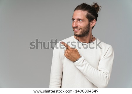 Happy young guy wearing casual clothing standing isolated over gray background, pointing finger at copy space