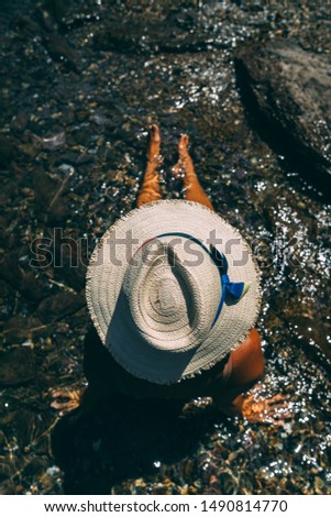 Young woman in white hat sitting in the water. View from top. Summer.