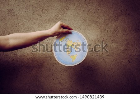 Flat Earth concept. Person who believes that Earth is flat disc. Anonymous woman holding flat Earth model in front of body with text: It`s flat. Isolated on gray background, studio shot. 