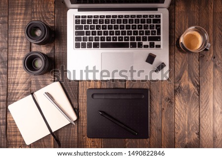 Top view of wooden desktop with laptop, table, coffee, notebook, mobile, memory cards. Photographer or designer using Laptop and tablet to edit.