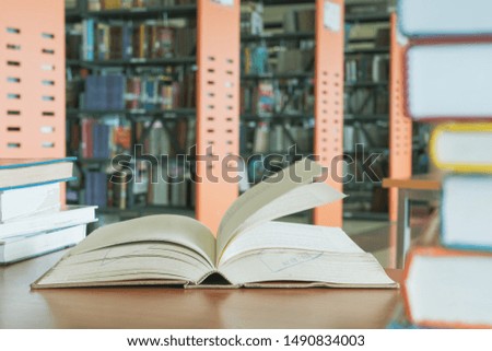 Open book in library with stack piles of literature text archive on wooden desk. Desk and Bookshelves in school library or study class use for learning and education concept.
