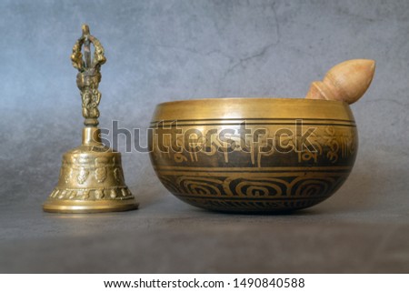 Singing bowl and golden bell close-up, soothing and meditative. Singing bowl with sanskrit engraving pattern and wooden mallet and golden bell of on gray background. Symbols of Asia