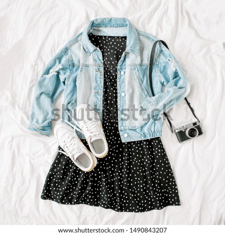 Blue jean jacket and  black dress with retro  photo camera on white bed. Women's stylish autumn or spring  outfit. Trendy clothes. Flat lay, top view.