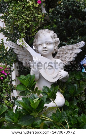 cupid play music statue on green leaf background in park