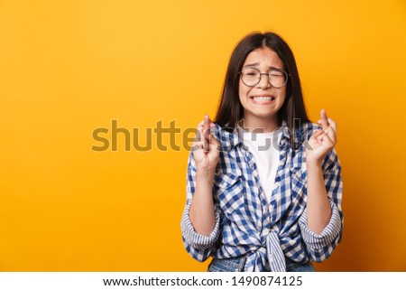 Picture of a nervous emotional young cute teenage girl in glasses posing isolated over yellow wall background showing hopeful please gesture.