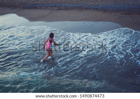lifestyle picture of girl in pink swimsuit running on the beach