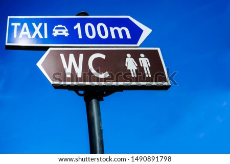 taxi and WC - inscription on signboard toilet through a hundred 100 meters hanging on a pole, a blue sky background. 