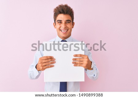 Young handsome businessman holding banner standing over isolated pink background with a happy face standing and smiling with a confident smile showing teeth