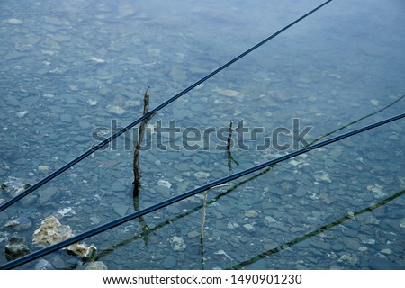 two fishing rods above smooth shallow water surface life style and hobby concept picture, background empty space for copy or text