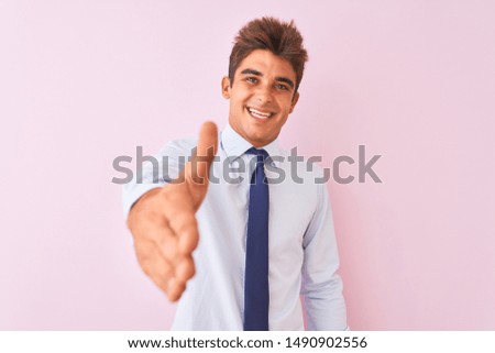 Young handsome businessman wearing shirt and tie standing over isolated pink background smiling friendly offering handshake as greeting and welcoming. Successful business.