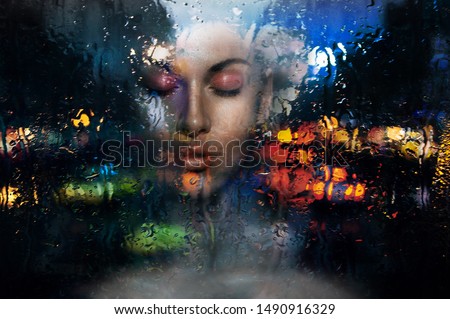 Romantic gothic sad dark hair open forehead pink make up face woman with closed eyes looks throw window on moistening rain fall in city with cars lights mirror effect on the glass in the night dark Royalty-Free Stock Photo #1490916329