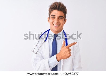 Young handsome doctor man wearing stethoscope over isolated white background cheerful with a smile of face pointing with hand and finger up to the side with happy and natural expression on face