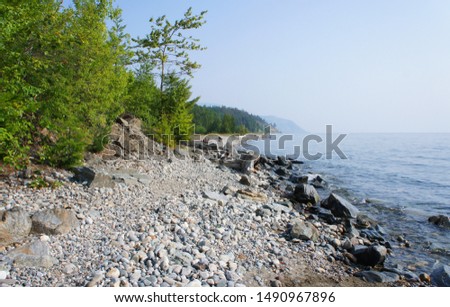 Wet stones and pebbles are in the foreground.Green trees and the blue expanse of Lake Baikal frame the picture
