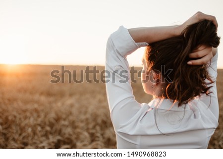 Young girl in wheat field at sunset. Curly-haired brunette white Caucasian girl watching the sunset in the field. Slow living life, mental health concept.