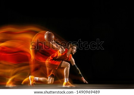 The comet. Young caucasian basketball player of red team in action and motion in mixed light over dark studio background. Concept of sport, movement, energy and dynamic, healthy lifestyle.