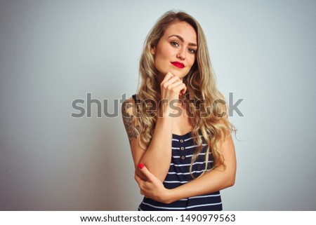 Young beautiful woman wearing stripes t-shirt standing over white isolated background looking confident at the camera smiling with crossed arms and hand raised on chin. Thinking positive.