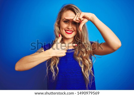 Young beautiful woman standing over blue isolated background smiling making frame with hands and fingers with happy face. Creativity and photography concept.